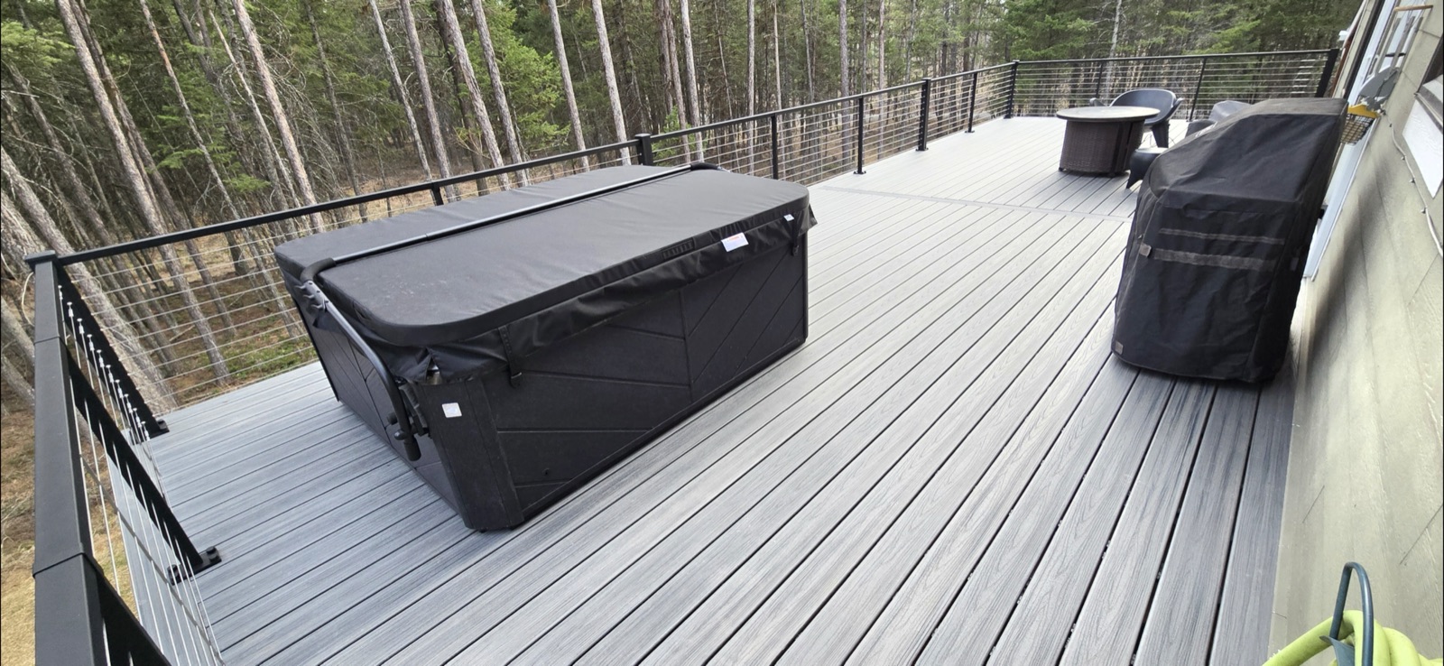 Composite hot tub deck with horizontal cable railing in a wooded Montana setting