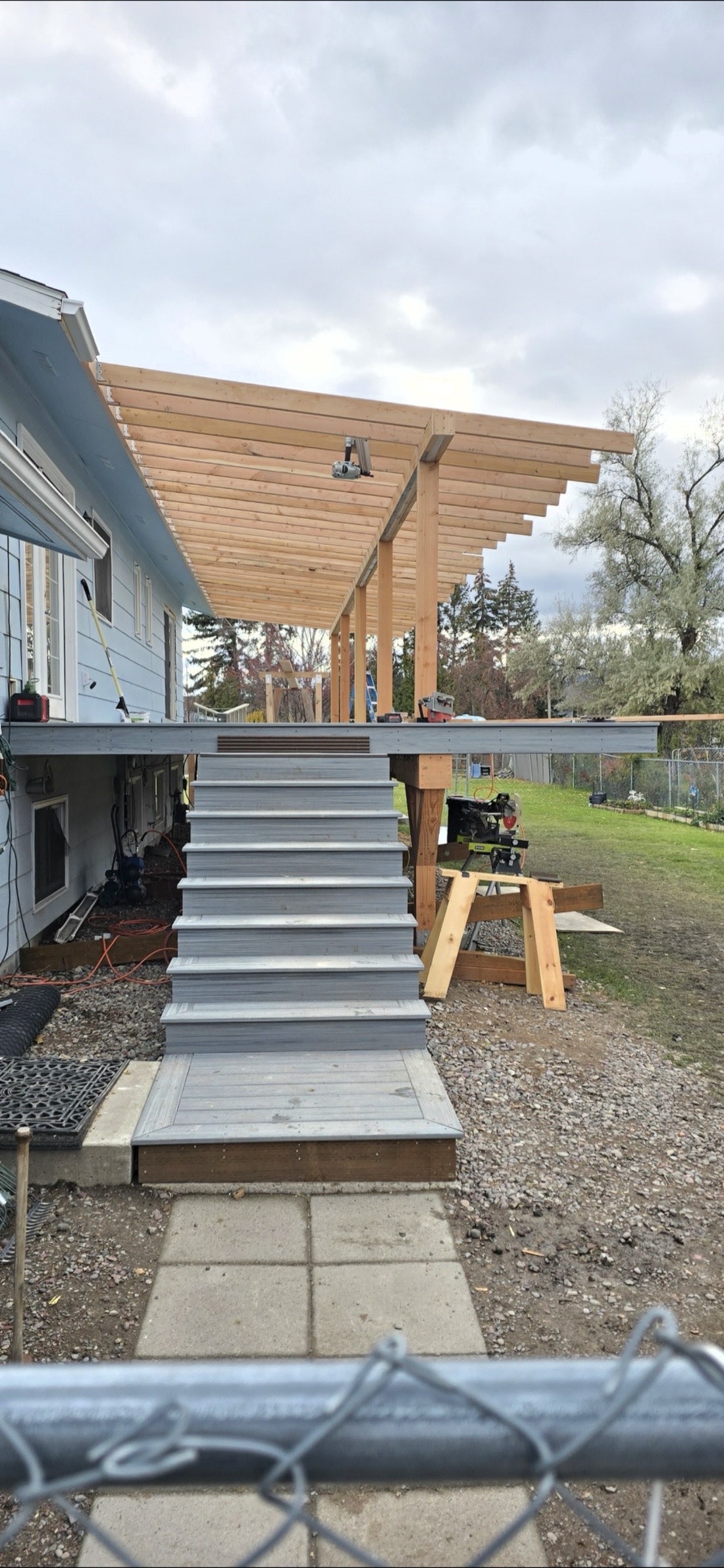Covered deck with new roof framing and gray composite stairs under construction in Montana