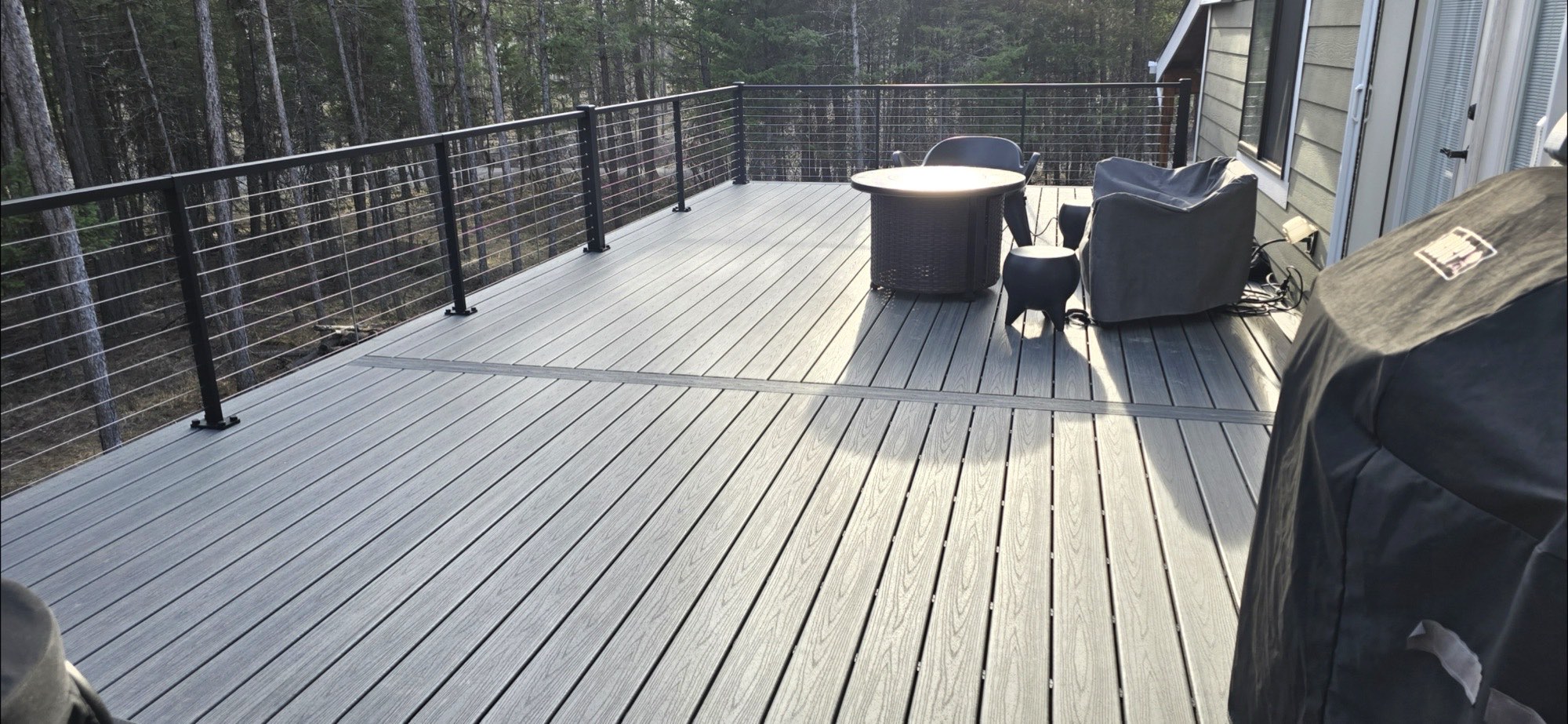 Finished gray composite deck with black cable railing overlooking pine forest in the Flathead Valley, Montana